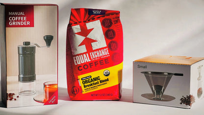 Three coffee-related products displayed side by side: a manual coffee grinder in its box on the left, a red Equal Exchange coffee bag in the center, and a small pour-over coffee kit in its box on the right, all photographed against a plain light background.